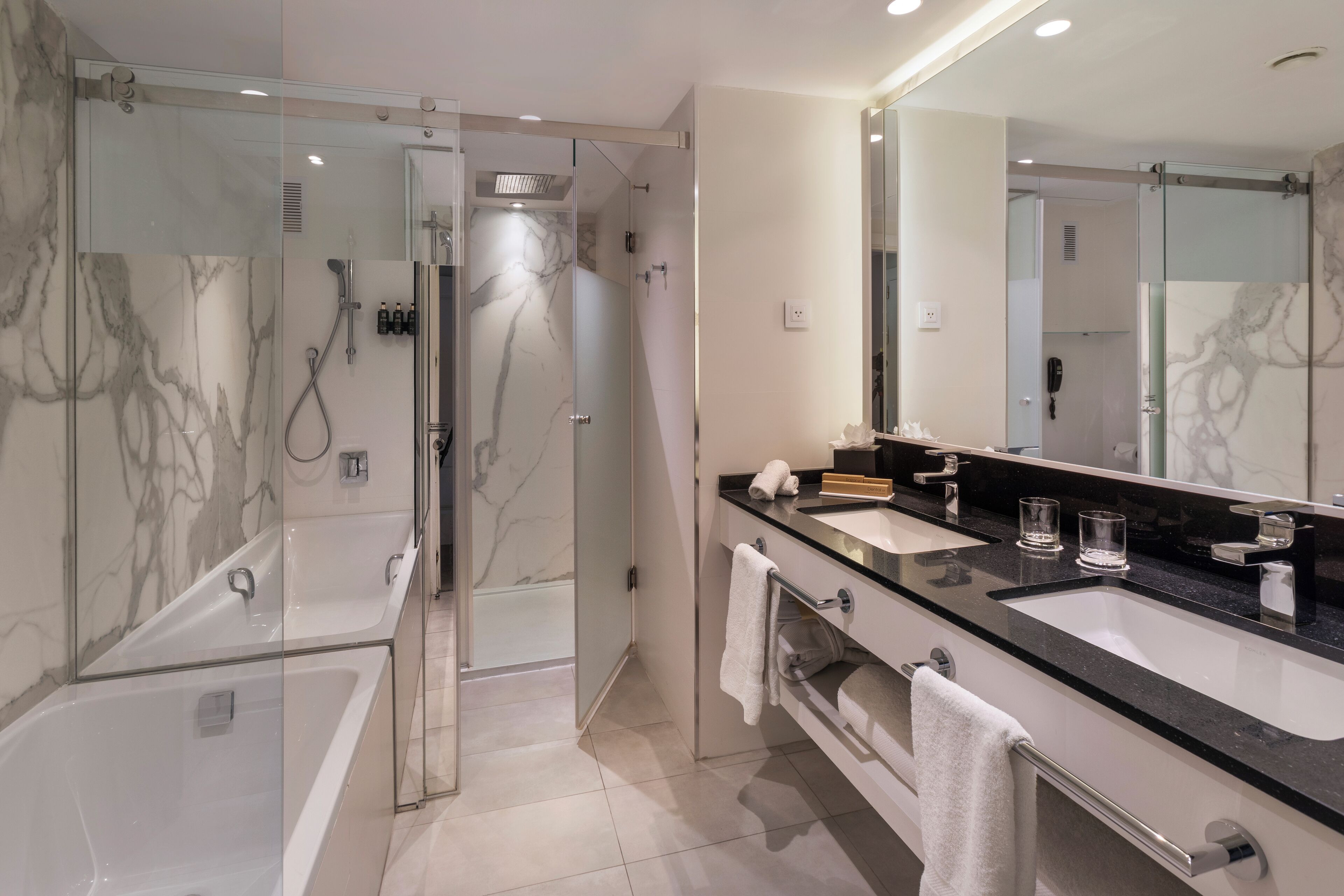 Un baño moderno con dos lavamanos, un espejo grande y una zona de ducha con mampara de vidrio.