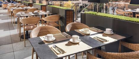 Un café en la azotea con terraza, que incluye sillas y mesas de mimbre, y vistas de la ciudad.