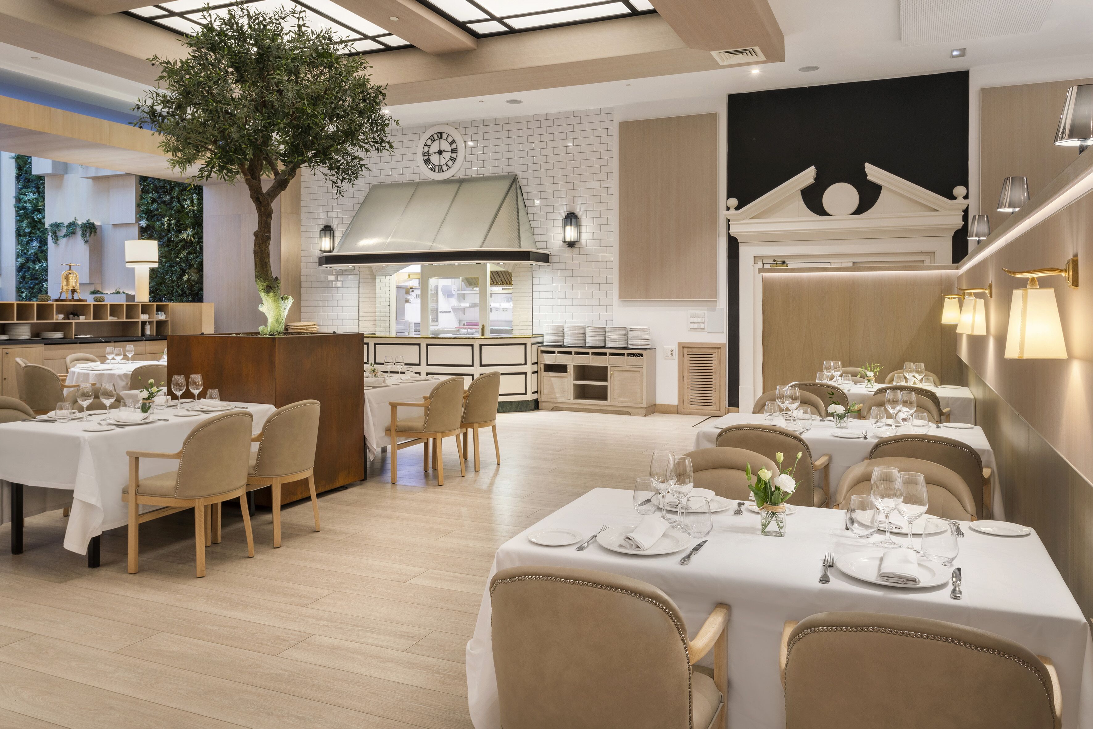 Un restaurante moderno con varias mesas, un árbol central y una zona de cocina.