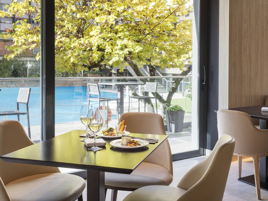 A dining area with a table set for two, a view of a swimming pool, and a tree outside the window.