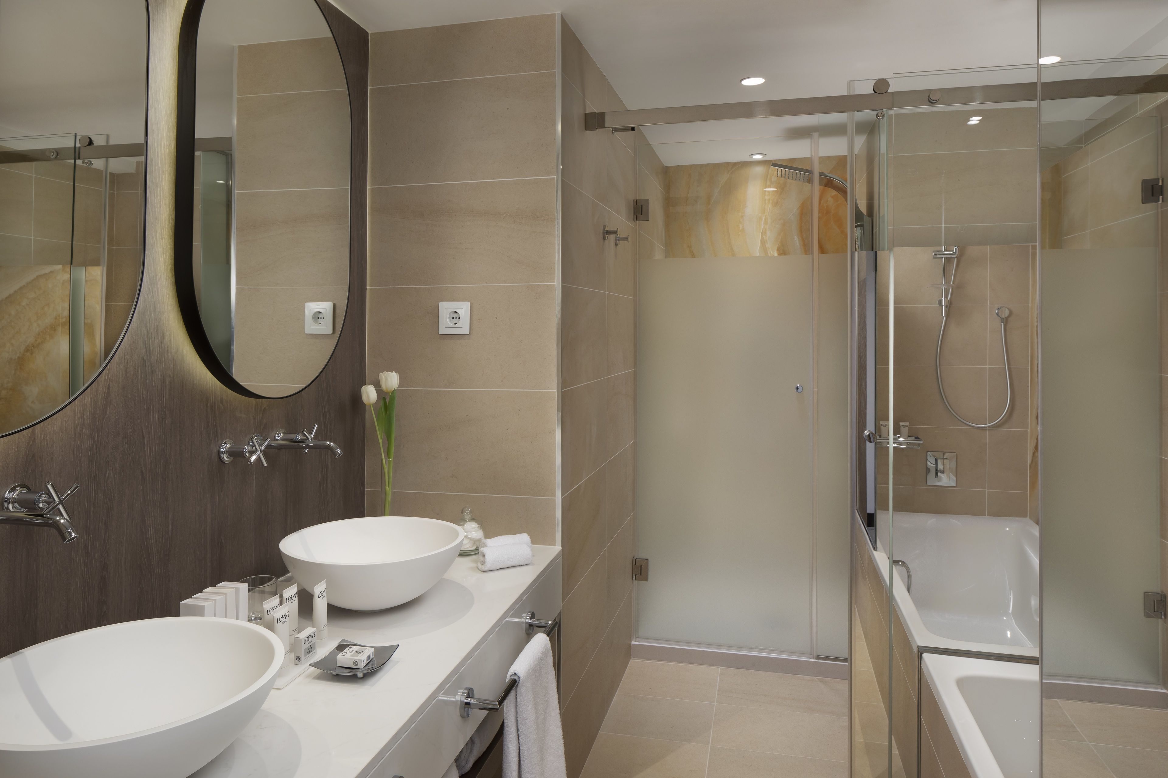 Un baño moderno con un espejo grande, dos lavamanos, una ducha y una bañera.
