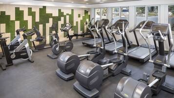 Un gimnasio con diversas máquinas de cardio, estaciones de pesas y una pared con diseño en verde y beige.