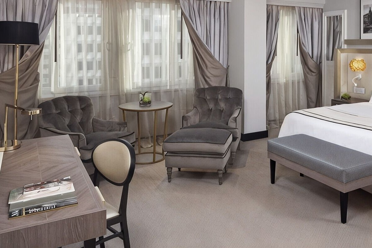 Una habitación de hotel con una cama, dos sillones, una mesita, un escritorio y una lámpara.