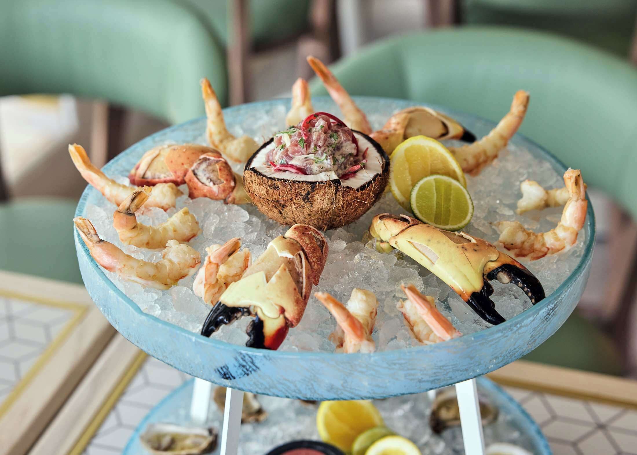 Un plateau de fruits de mer comprenant des crevettes, des pinces de crabe et un plat principal servi sur de la glace, le tout agrémenté de quartiers de citron vert.