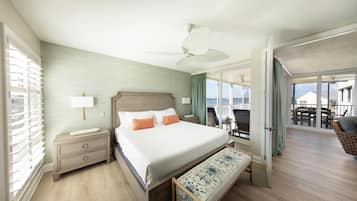 Habitación de hotel con una cama grande, una mesita de noche, un banco, un ventilador de techo y vistas al balcón.