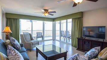 A spacious living room with a sofa set, a glass coffee table, a television, and a ceiling fan.
