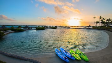 A beach with kayaks and thatched-roof structures.