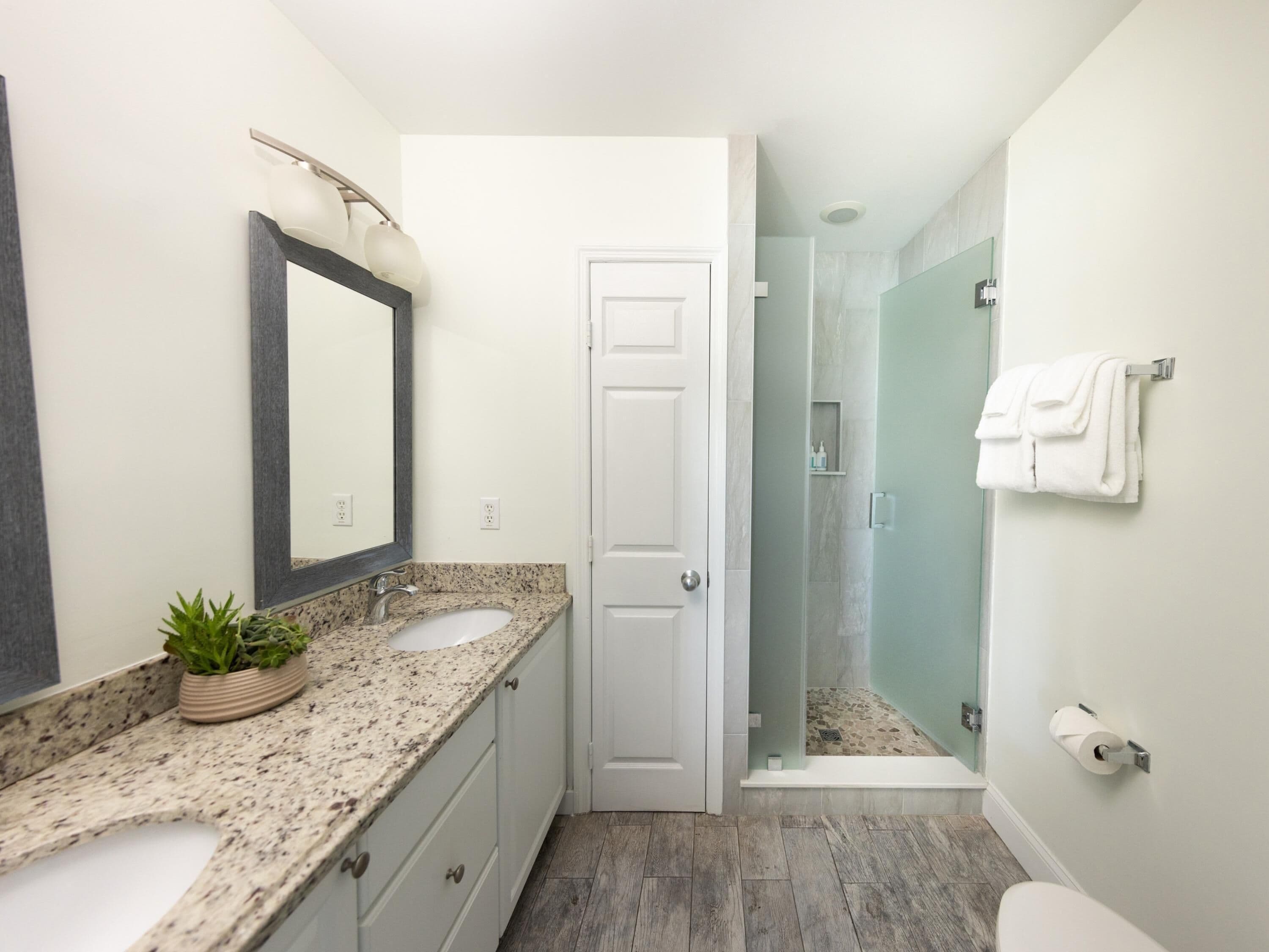 Une salle de bain moderne avec un lavabo surmonté d’un plan de travail en granit, un grand miroir, une douche avec une porte en verre et des toilettes.