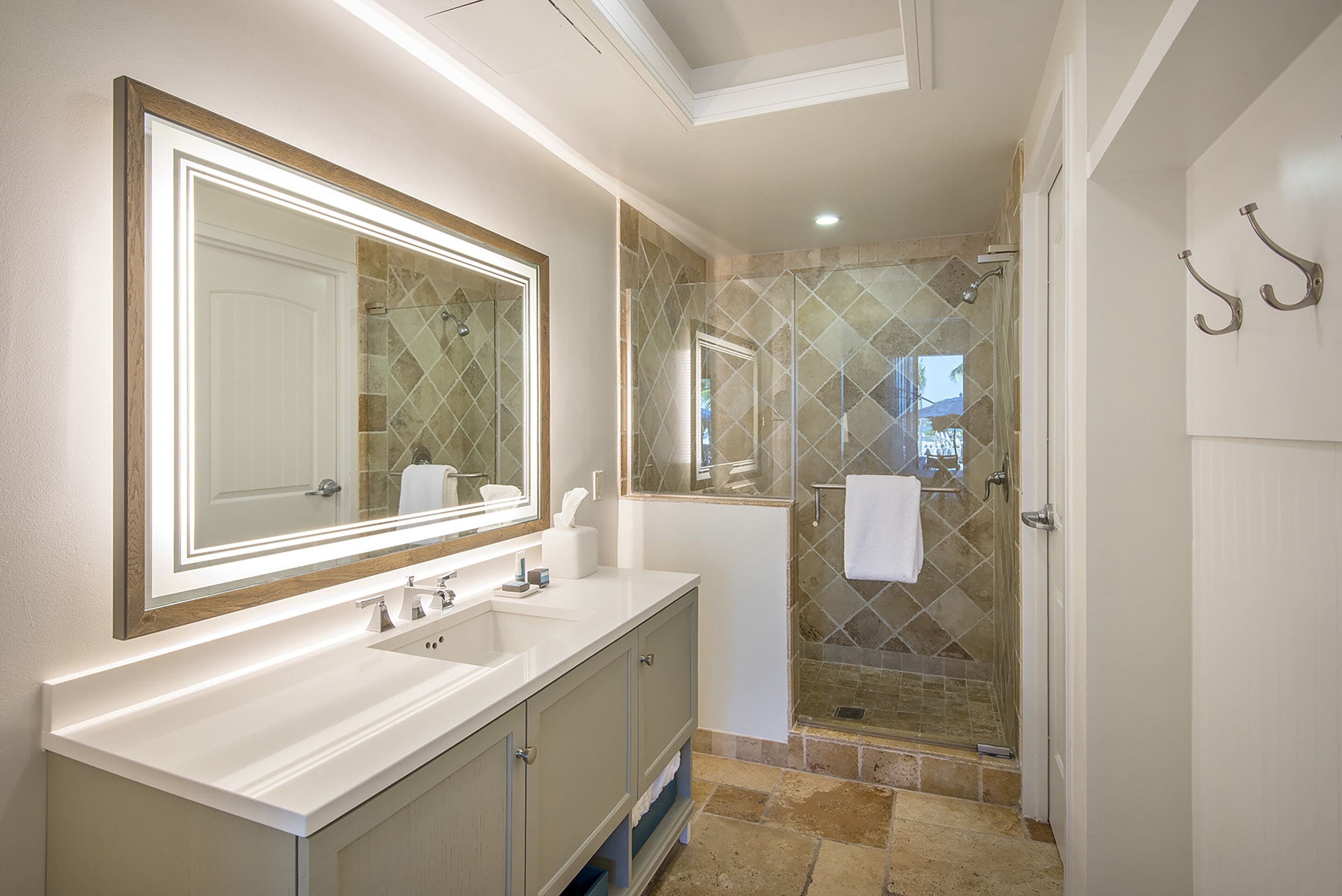 A bathroom with a large mirror, two sinks, a shower with glass doors, and a towel rack.