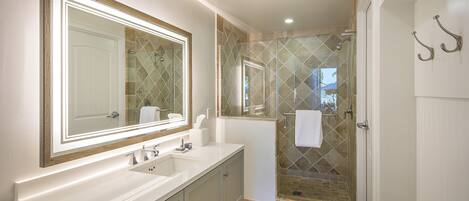 A bathroom with a large mirror, two sinks, a shower with glass doors, and a towel rack.