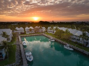 A resort with a central pool, connected by walkways to multiple bungalow-style buildings, surrounded by palm trees and a sunset view. - Hawks Cay Resort (Marathon)