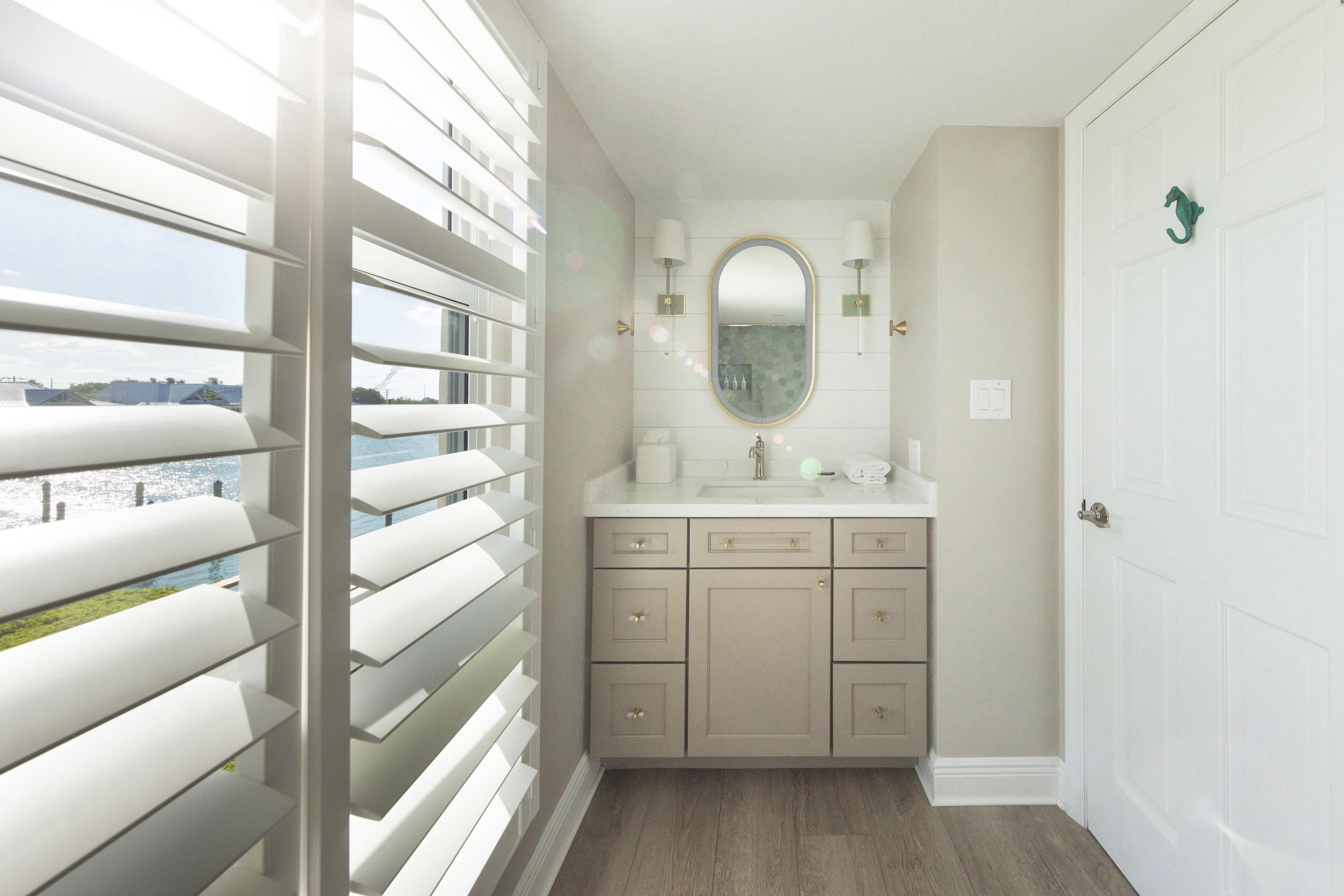 A bathroom with a large window, a sink, and a mirror.