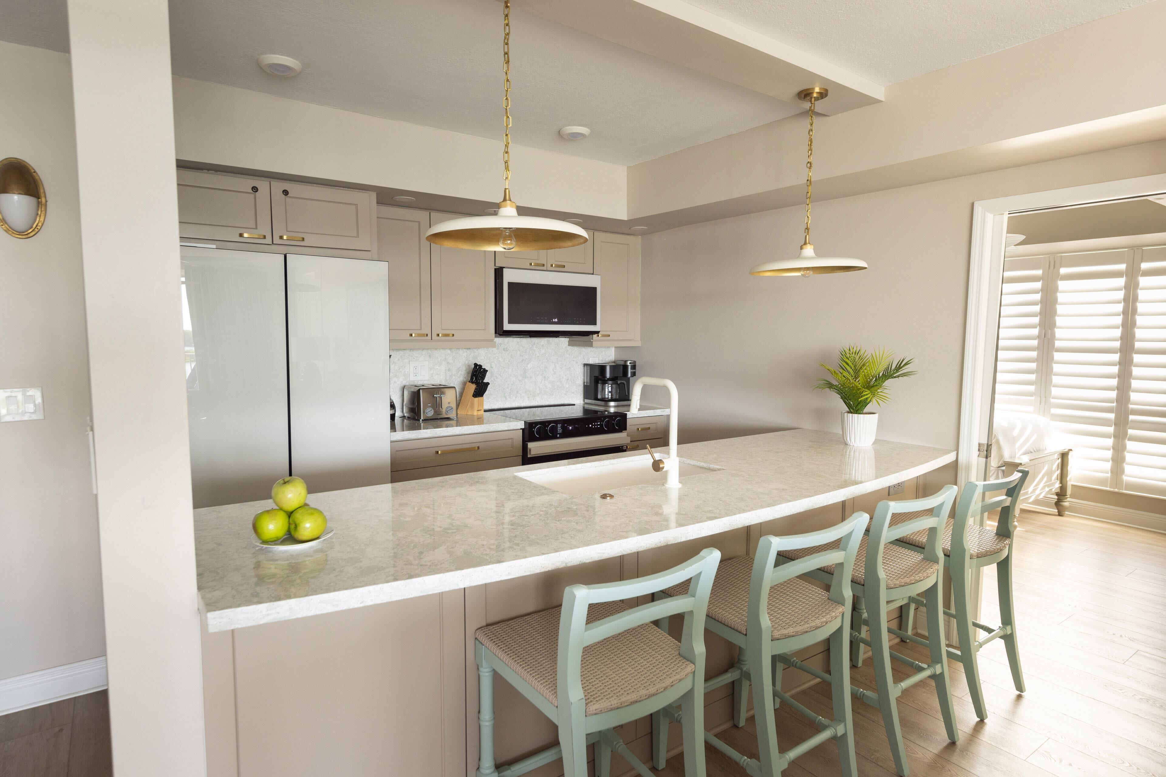 A modern kitchen with a central island, bar stools, a microwave, and a sink.