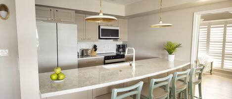 A modern kitchen with a central island, bar stools, a microwave, and a sink.