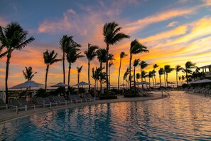 A poolside area with lounge chairs and umbrellas, surrounded by palm trees, during sunset. - Hawks Cay Resort (Marathon)