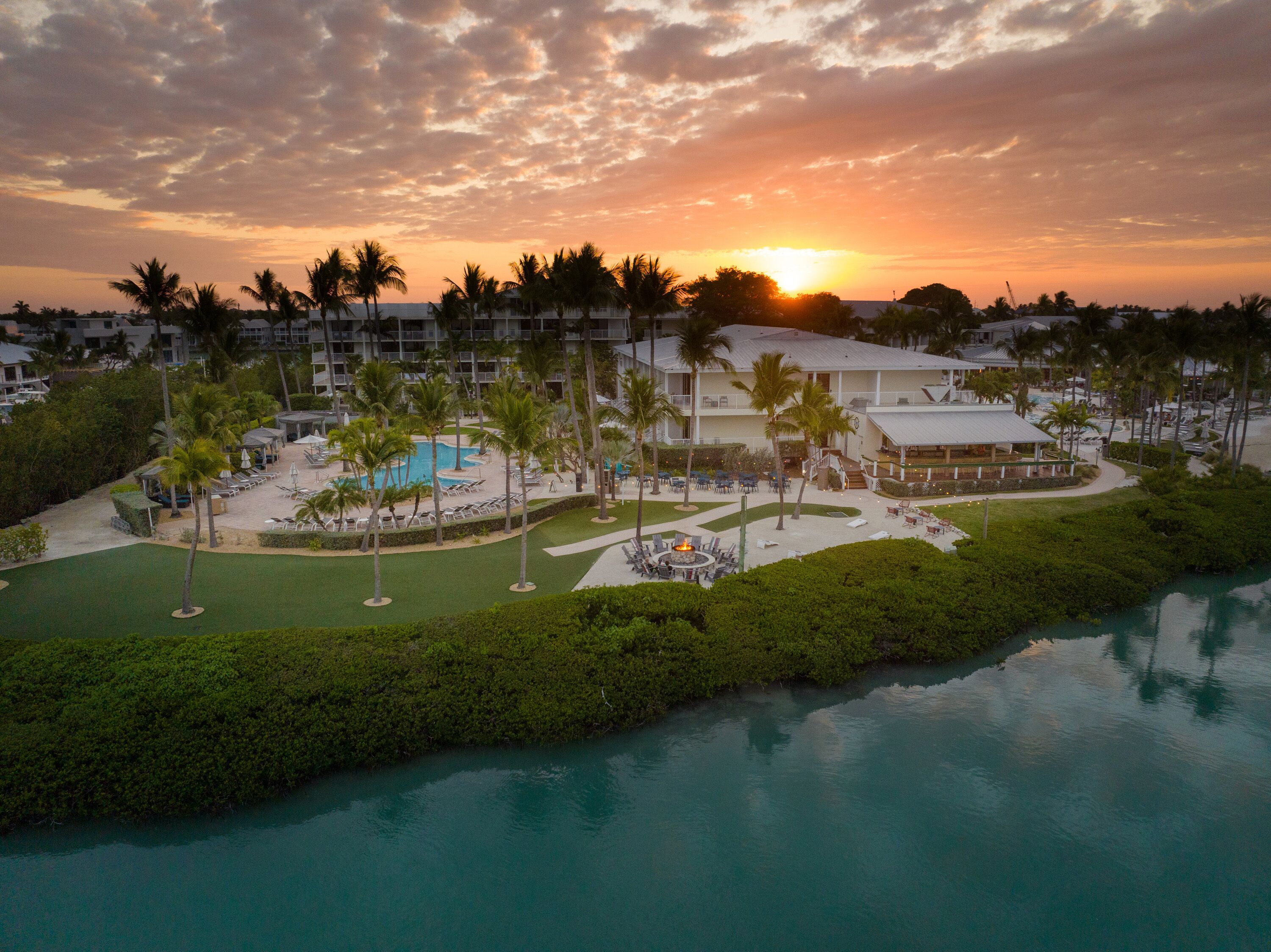 Un resort con piscina, palmeras y vistas al atardecer.