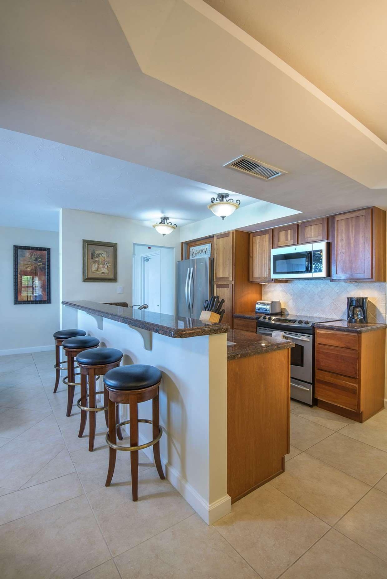 A modern kitchen with a central island, bar stools, stainless steel appliances, and wooden cabinetry.