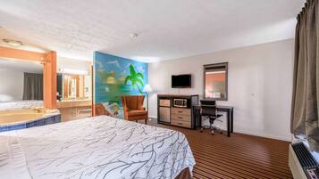 Une chambre d’hôtel avec un lit, un bureau, une chaise, une télévision, un tableau et une salle de bain visible à travers une porte ouverte.