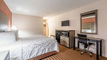 A hotel room with a bed, a desk, a chair, a television, and a microwave.