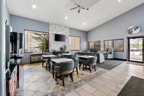 A modern dining area with multiple tables and chairs, a flat-screen TV mounted on the wall, and a ceiling fan.