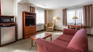 A hotel room with a television, a small refrigerator, a sofa, a chair, a table, and a lamp.