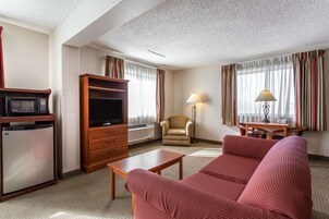 Habitación de hotel con televisión, refrigerador pequeño, sofá, sillón, mesa y lámpara.