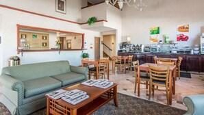 A hotel lobby with a sofa, dining area, kitchen, and a reception desk.