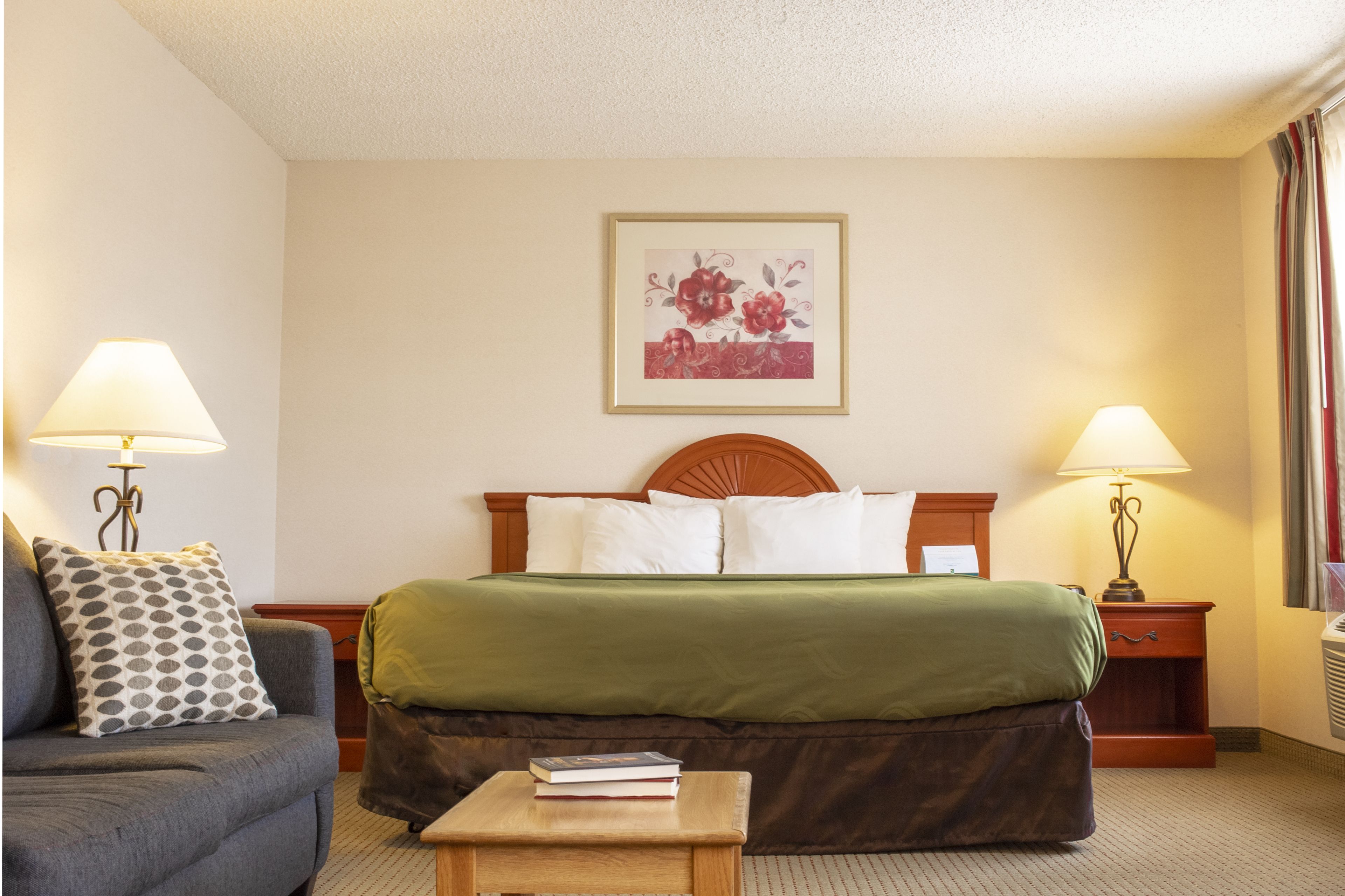 A hotel room with a bed, a couch, two nightstands, a lamp, and a framed floral artwork on the wall.