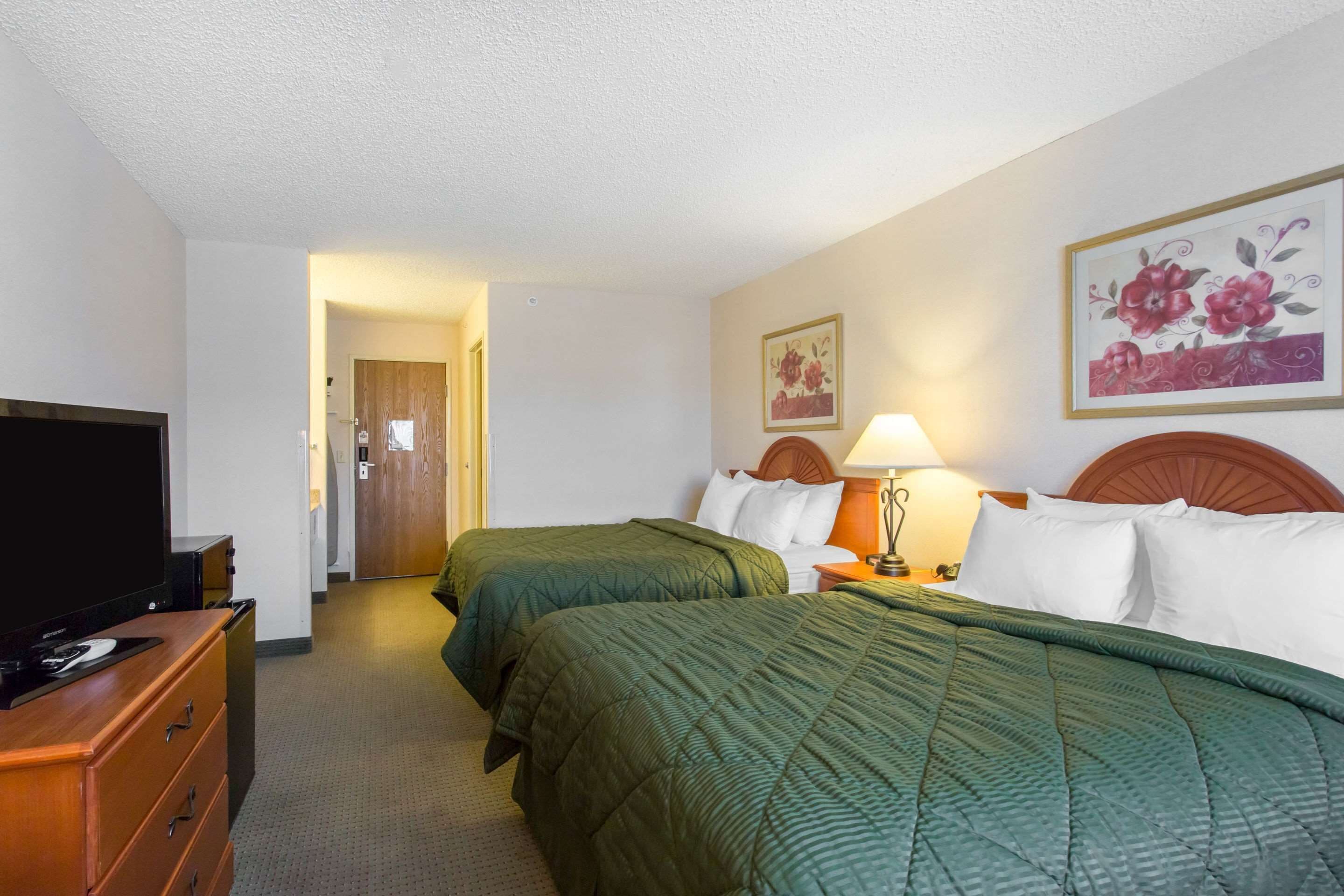 A hotel room with two beds, a TV, a dresser, and artwork on the walls.