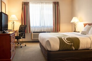 A hotel room with a bed, a desk with a TV, two lamps, a chair, and a window with curtains. - Quality Inn Delta Gateway to Rocky Mountains (Delta)