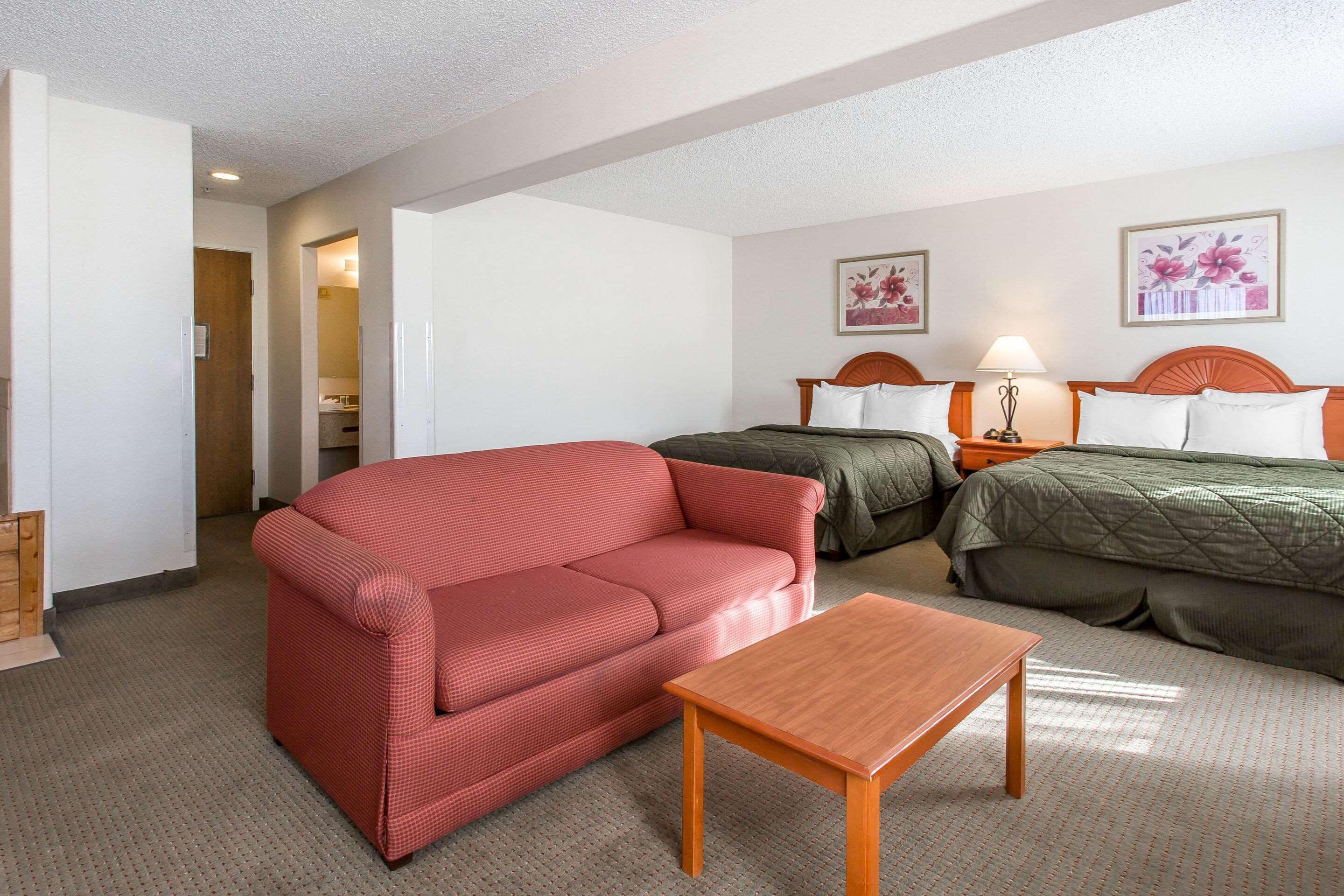 A hotel room with a red sofa, a wooden table, two beds with green and white bedding, and two framed floral pictures on the wall.