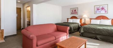 A hotel room with a red sofa, a wooden table, two beds with green and white bedding, and two framed floral pictures on the wall.