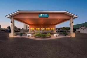 A hotel with a covered entrance, outdoor seating, and a sign for Quality Inn by Choice Hotels.