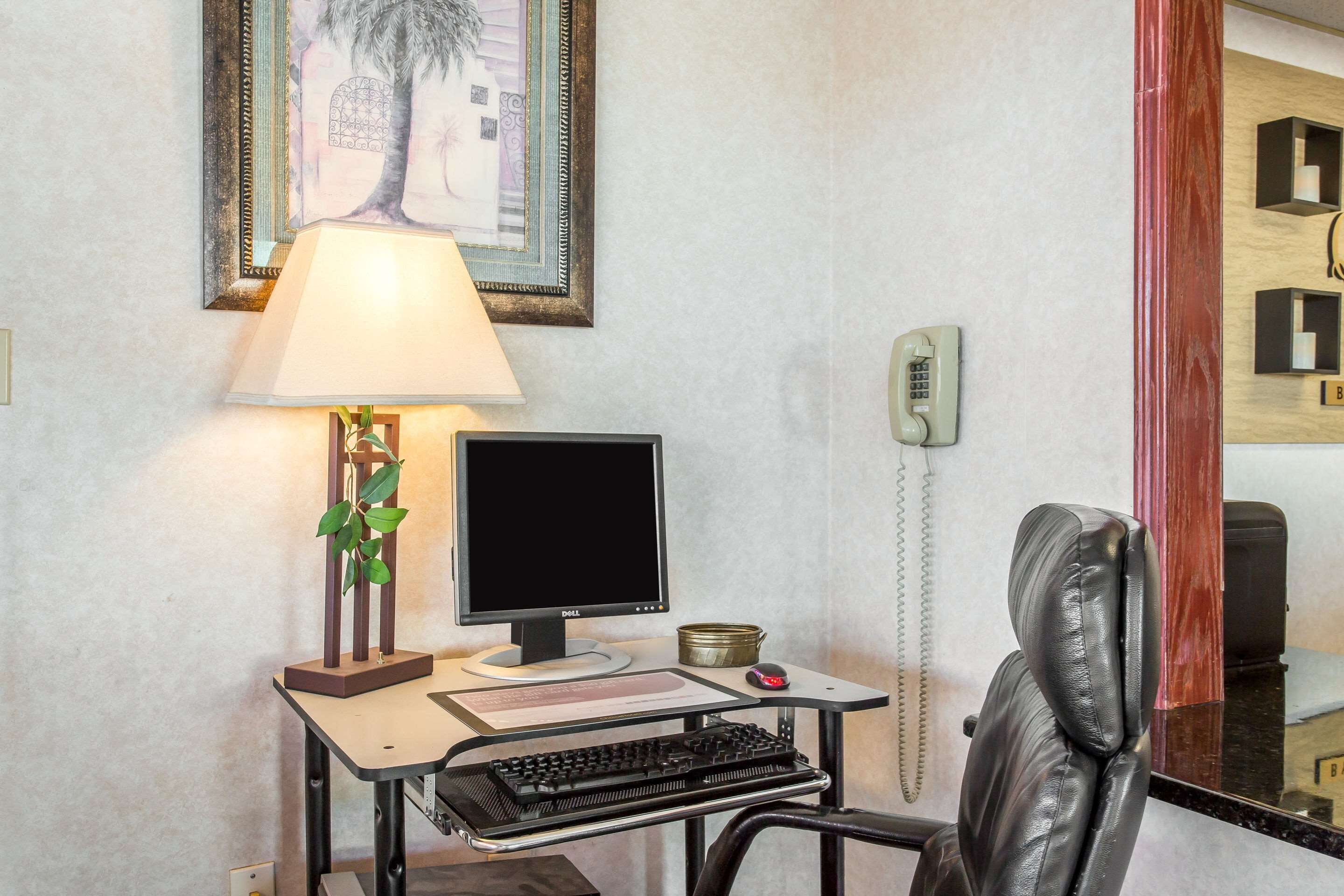Un bureau avec un ordinateur, un clavier et une souris, une lampe, un tableau encadré et un téléphone.