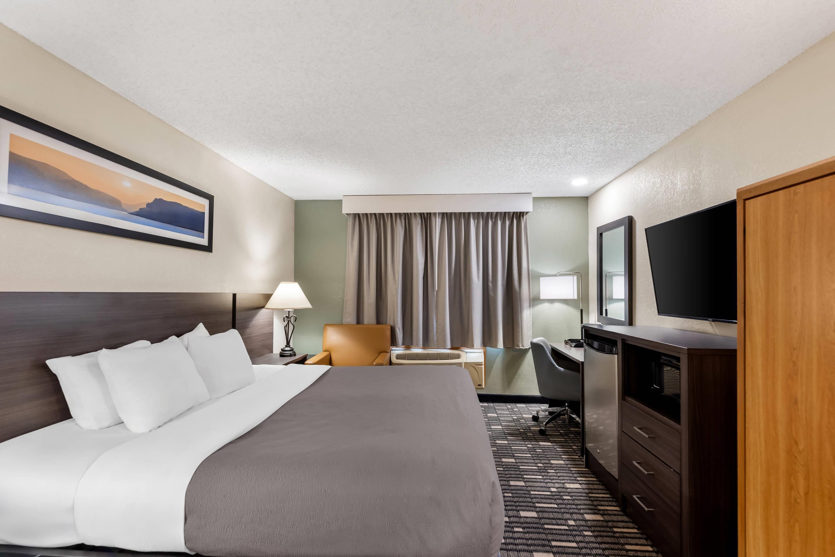 A hotel room with a large bed, a desk, a chair, a television, and a painting on the wall.