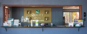 Mostrador de recepción en Quality Inn con estructura de madera, un cartel y varios folletos informativos.