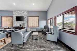 Un'area lounge moderna con posti a sedere, una TV a schermo piatto e ampie finestre con tende.