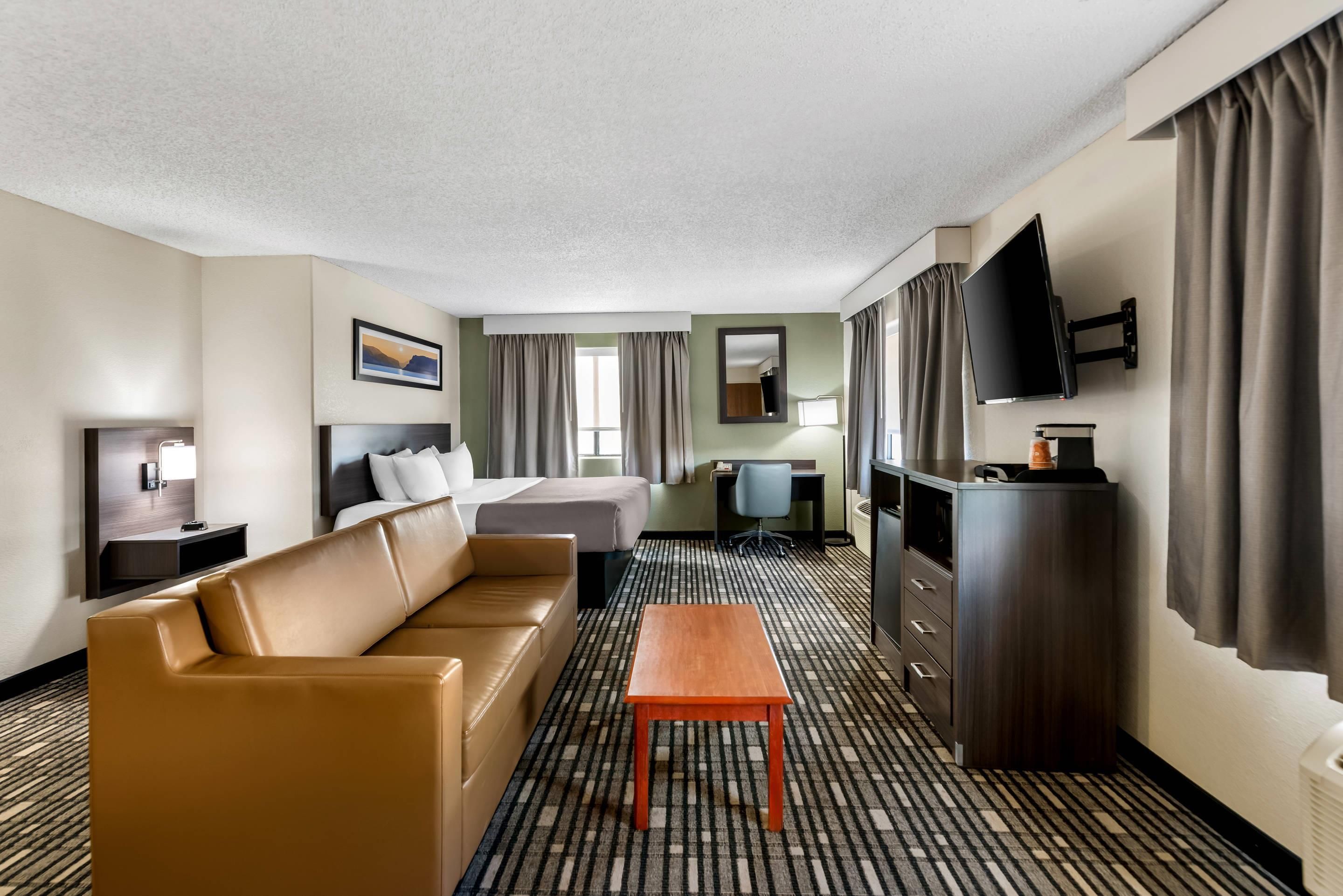 A hotel room with a sofa, a bed, a desk, a television, and a mirror.