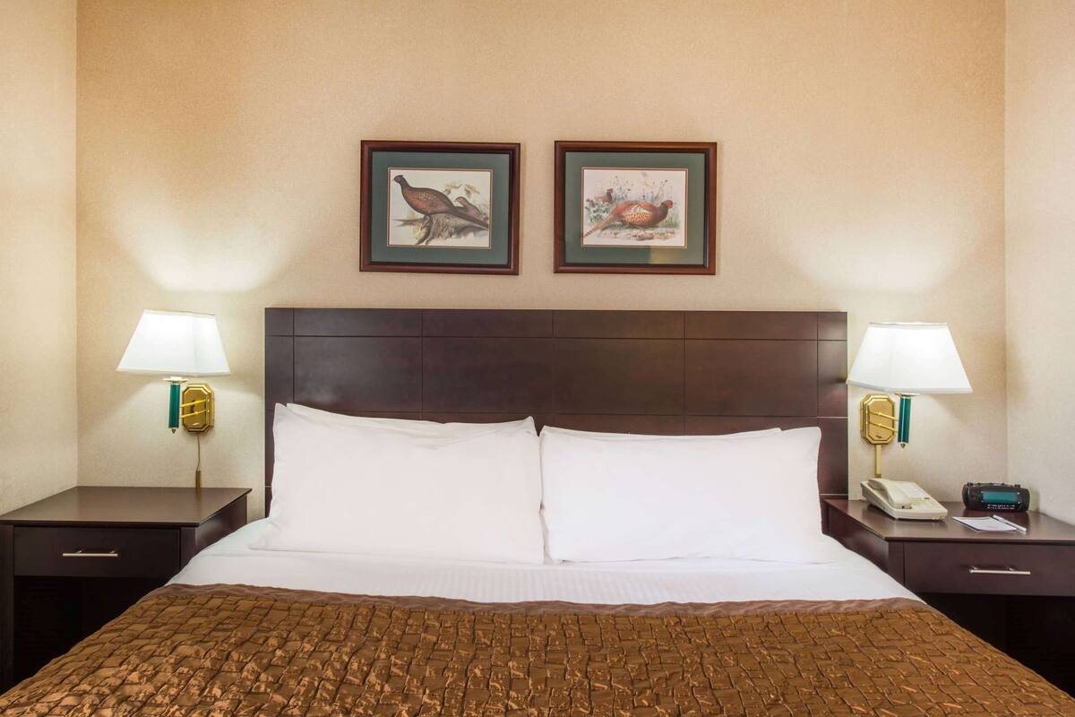 A hotel room with a large bed, two nightstands, a wooden headboard, and two framed pictures on the wall.