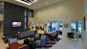 A spacious lobby with a modern design, featuring a large flat-screen TV, comfortable seating areas, and a view of the outside through large windows.