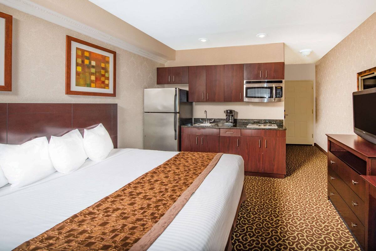 A hotel room with a bed, a kitchenette, and a television.