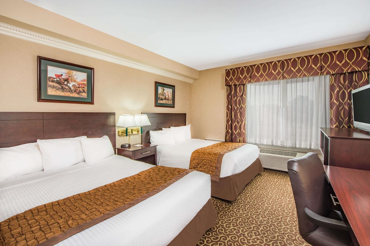 A hotel room with two beds, a desk, a chair, a TV, and two framed pictures on the wall.