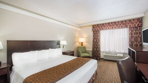A hotel room with a large bed, a desk, a chair, a TV, and a window with curtains.