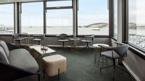 A modern conference room with large windows, grey upholstered chairs, a central table with a candle, and a view of the sea and boats.