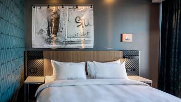 A modern hotel room with a large bed, a headboard with a textured design, a wall-mounted artwork, and a small bedside table.