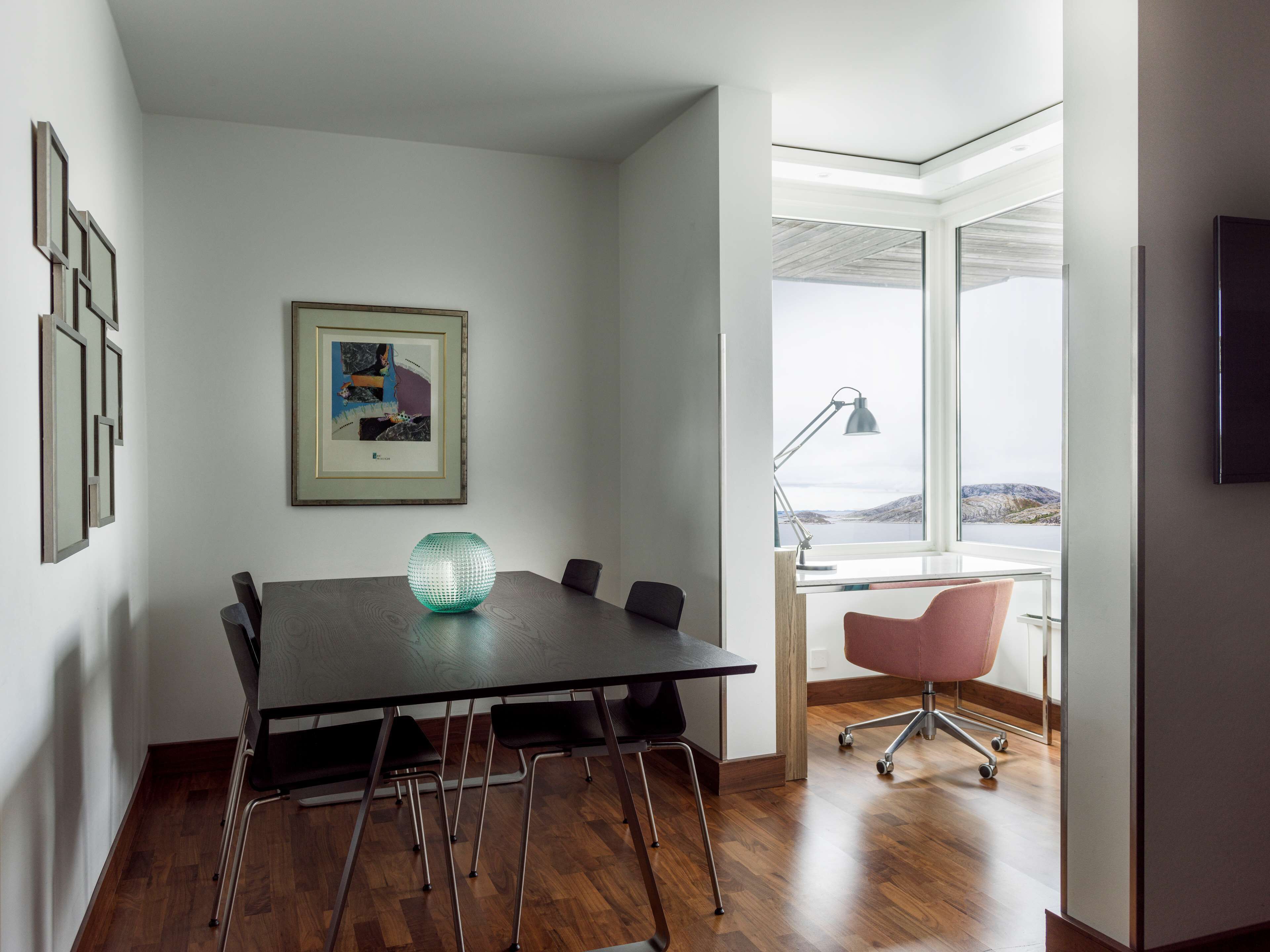 A modern meeting room with a large table, chairs, a framed picture, and a view of a lake through large windows.