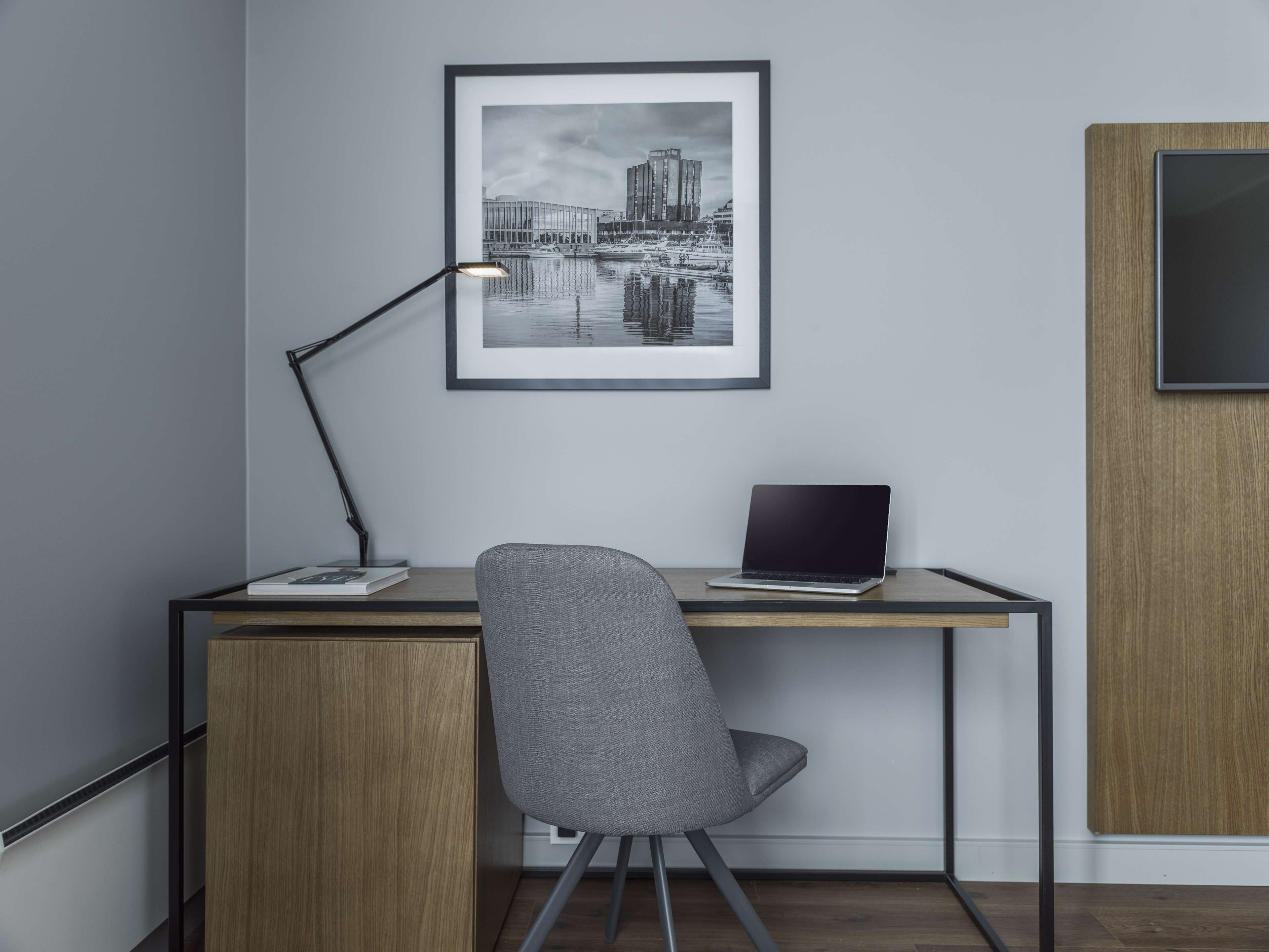 Un espacio de oficina moderno con un escritorio, una silla, una computadora portátil y una fotografía enmarcada de un paisaje urbano en la pared.