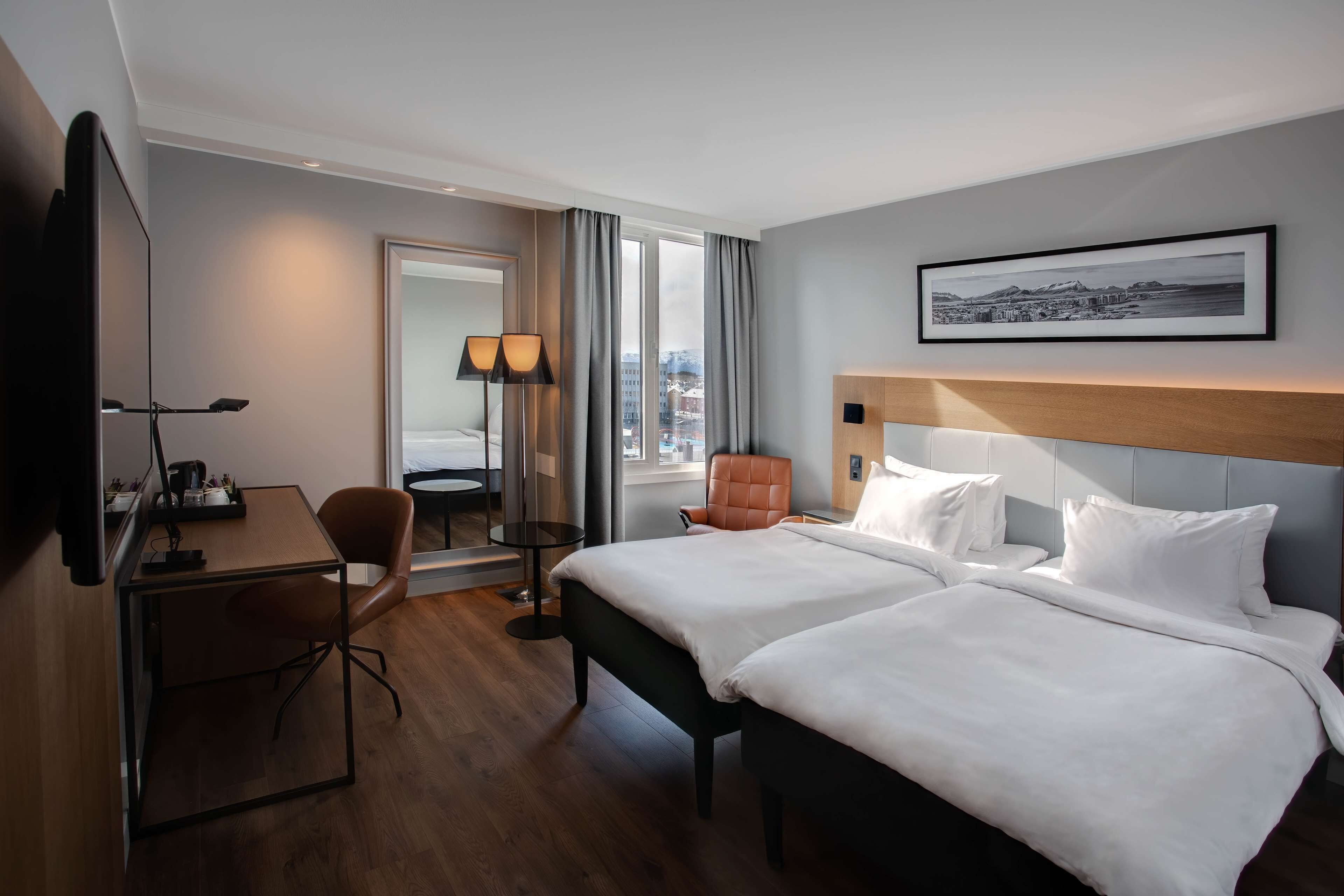 Habitación de hotel con una cama grande, un escritorio, una silla y vista a la ciudad por la ventana.
