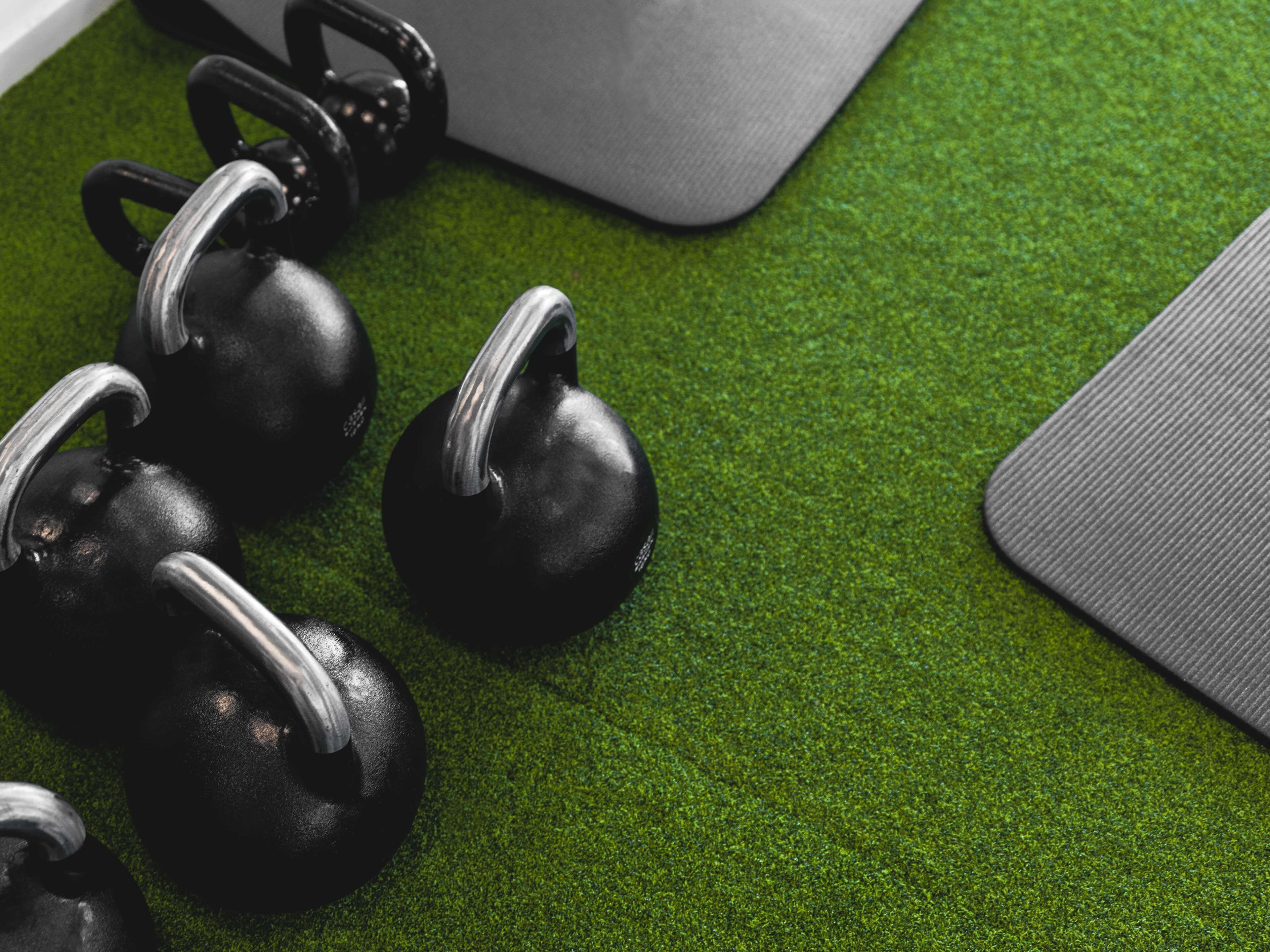 A green exercise mat with black kettlebells on a textured surface.
