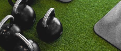 A green exercise mat with black kettlebells on a textured surface.